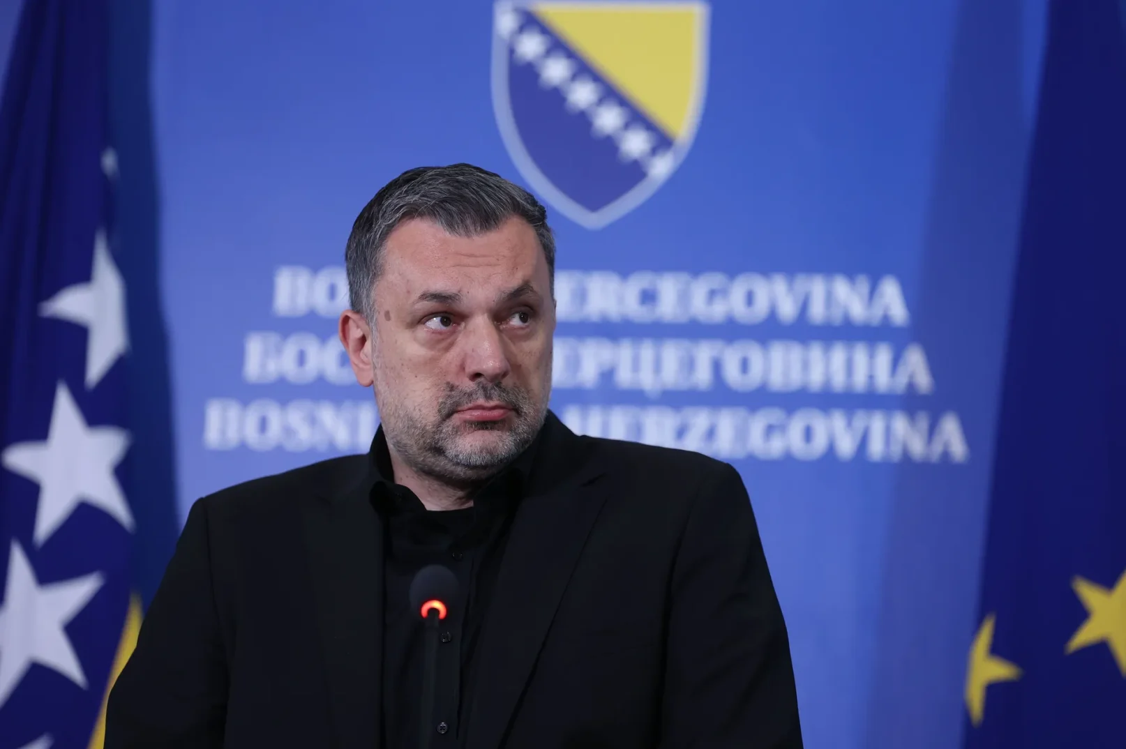 Ministar u crnom odijelu stoji ispred zastave Bosne i Hercegovine