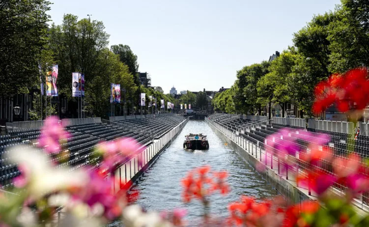 Brod plovi kanalom u Amsterdamu, okružen tribinama i zastavama.