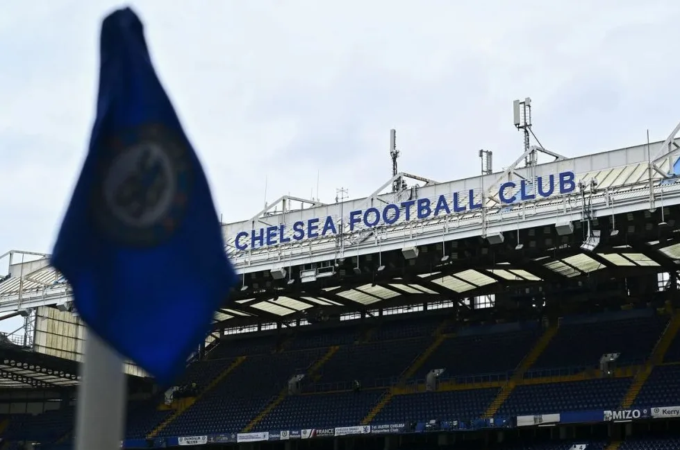 Plava zastava s grbom Chelsea FC ispred stadiona sa natpisom "CHELSEA FOOTBALL CLUB"
