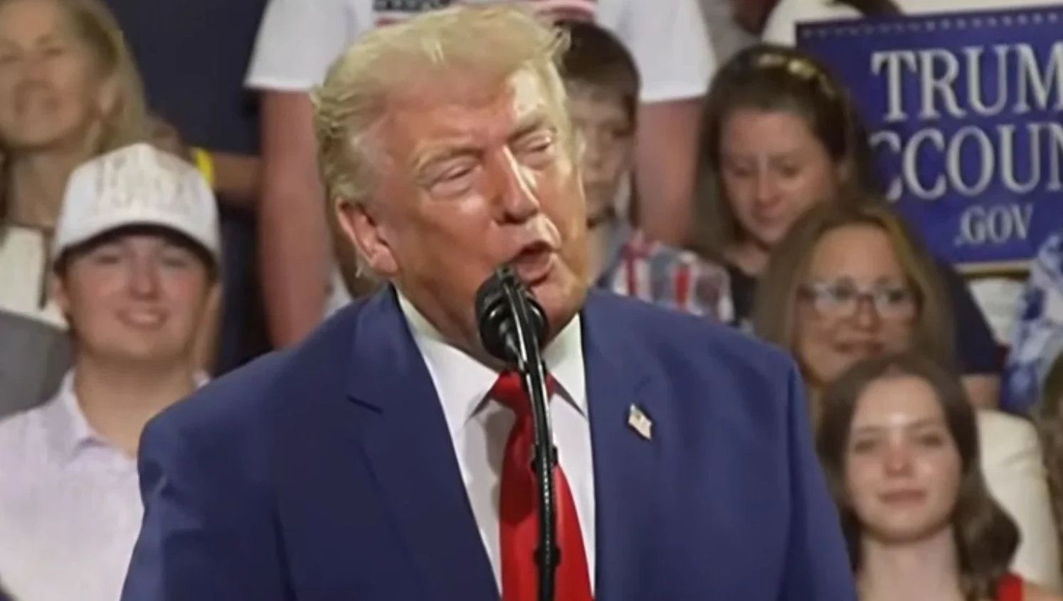 Donald Trump govori u mikrofon na skupu, s publikom u pozadini.