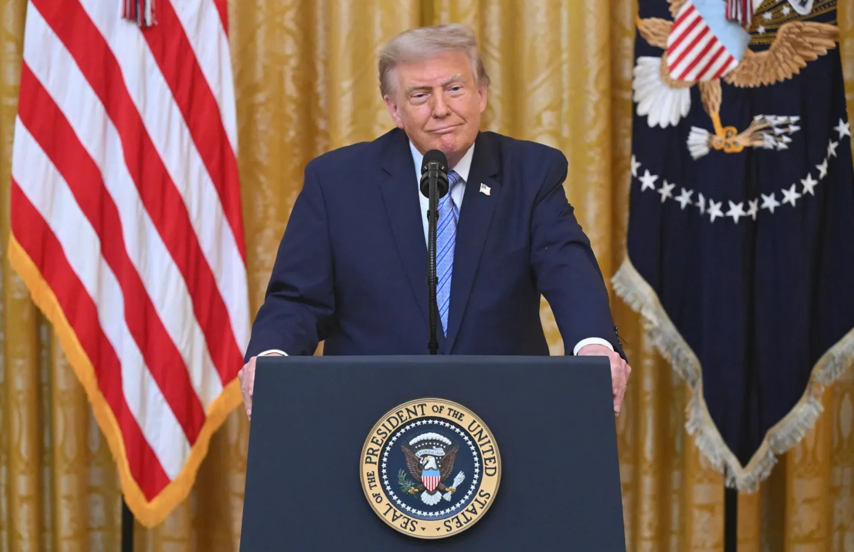 Donald Trump stoji iza predsjedničke govornice u Bijeloj kući, sa američkom zastavom lijevo i predsjedničkom zastavom desno.