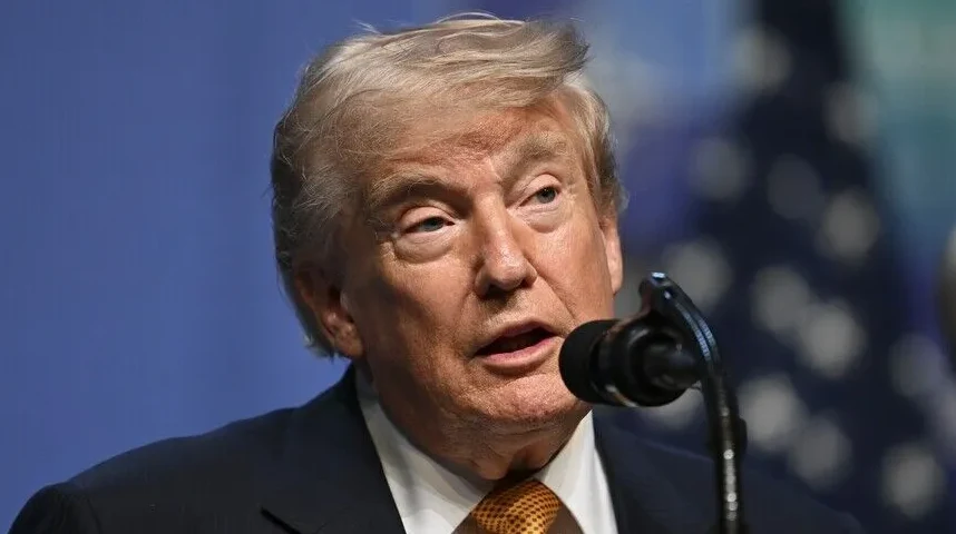 Donald Trump u crnom odijelu i žutoj kravati govori u mikrofon.