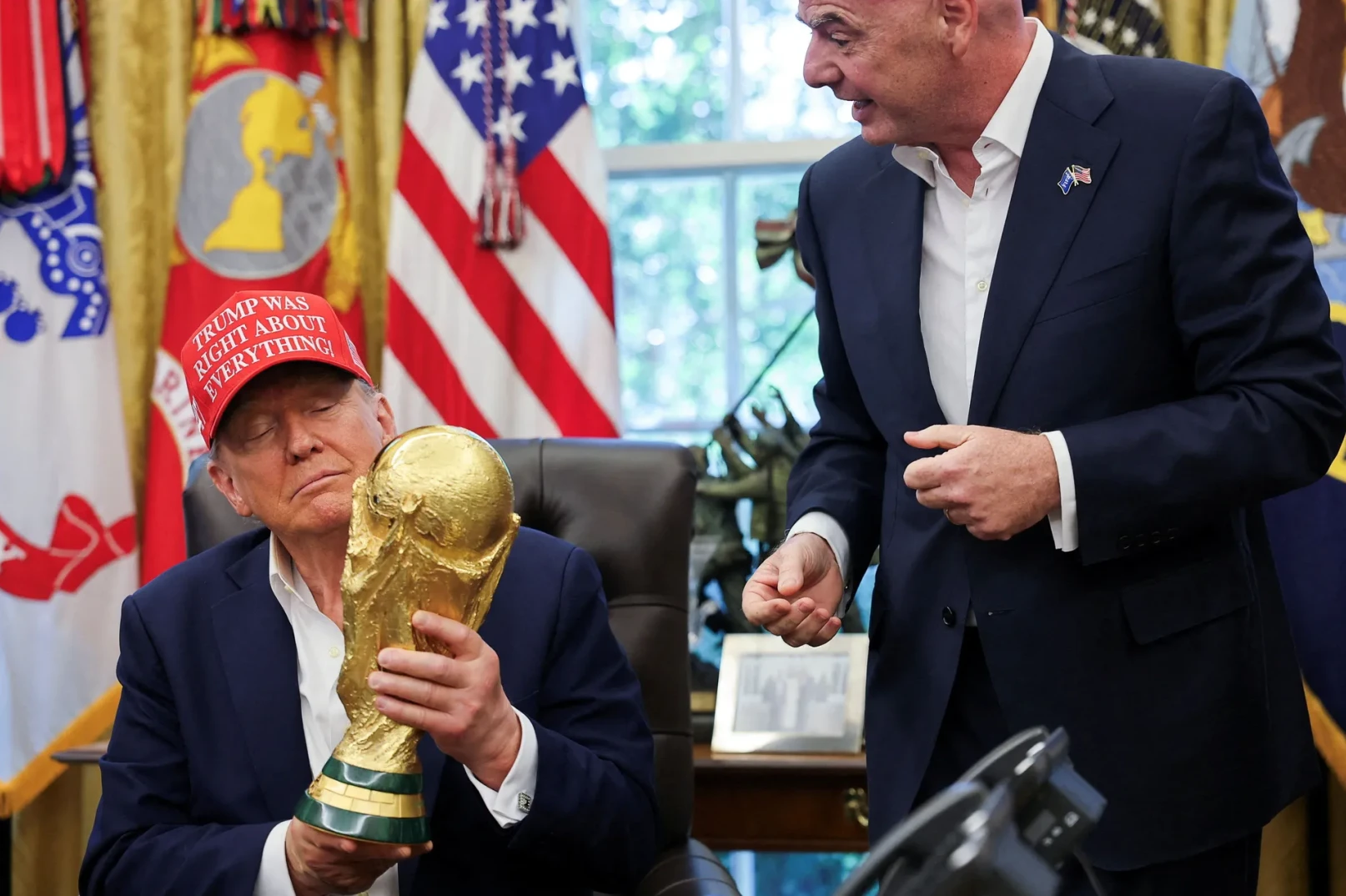 Donald Trump u Ovalnom uredu sa crvenom kapom na kojoj piše "TRUMP WAS RIGHT ABOUT EVERYTHING!" drži Zlatni trofej Svjetskog prvenstva.
