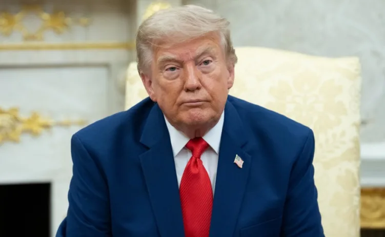 Donald Trump sjedi u plavom odijelu i crvenoj kravati, gledajući direktno u kameru.