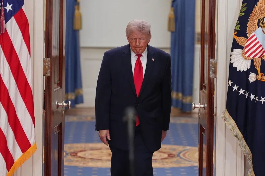 Donald Trump u tamnom odijelu i crvenoj kravati ulazi kroz vrata Bijele kuće, spuštene glave.