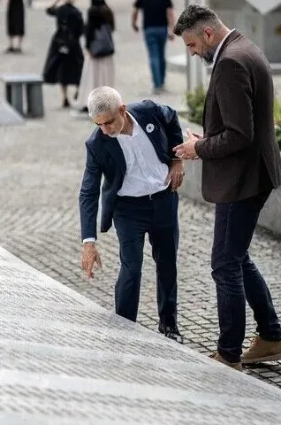 Dva muškarca u tamnim odijelima pregledavaju natpis na kamenom stepeništu.