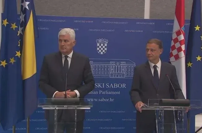 Dva muškarca u odijelima stoje za podijem ispred zastava Europske unije, Bosne i Hercegovine i Hrvatske, uz natpis "HRVATSKI SABOR" i "Croatian Parliament".