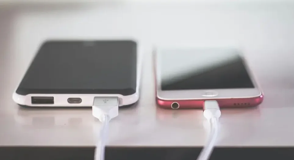 Dva pametna telefona, jedan crni i jedan crveni, su povezana na punjenje pomoću bijelih USB kablova.