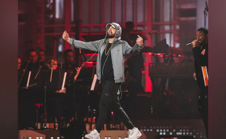 Eminem izvodi pjesmu na bini sa reperom pored njega i orkestrom u pozadini.