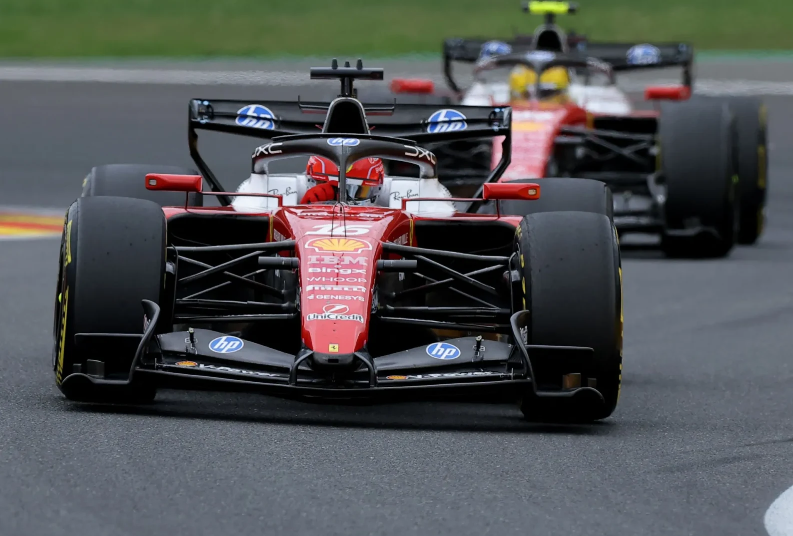Dva bolida Formule 1 se takmiče na mokroj stazi, u prvom planu je crveni bolid sa brojem 16.