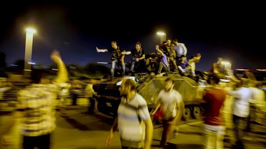 Grupa ljudi slavi na tenku i oko njega noću, neki od njih mašu rukama.