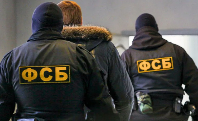 Dva agenta Federalne službe sigurnosti (FSB) u crnim uniformama s ruskim grbom na leđima, prate osobu obučenju u jaknu s krznenom kragnom.