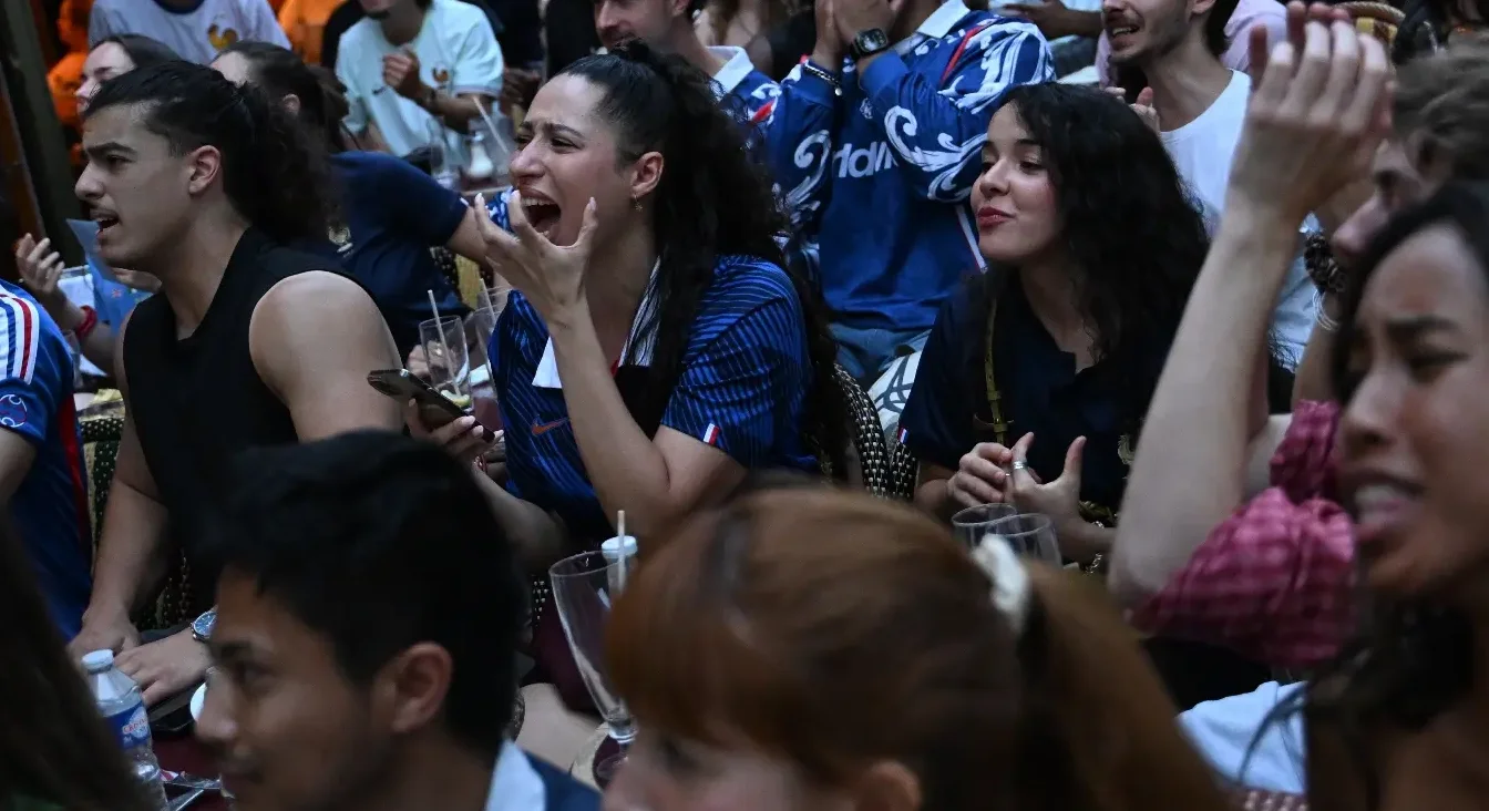 Grupa navijača u plavim dresovima, koji vjerovatno predstavljaju Francusku, izražavaju snažne emocije tokom gledanja fudbalske utakmice.