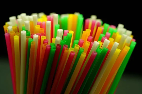 Približni prikaz gomile šarenih plastičnih slamčica za piće, crvenih, zelenih, žutih, narančastih i bijelih, na tamnoj pozadini.