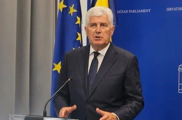 Gospodin u tamnom odijelu i bijeloj košulji s tamnom kravatom govori iza stalka s mikrofonom, sa zastavom Evropske unije i zastavom Hrvatske u pozadini.