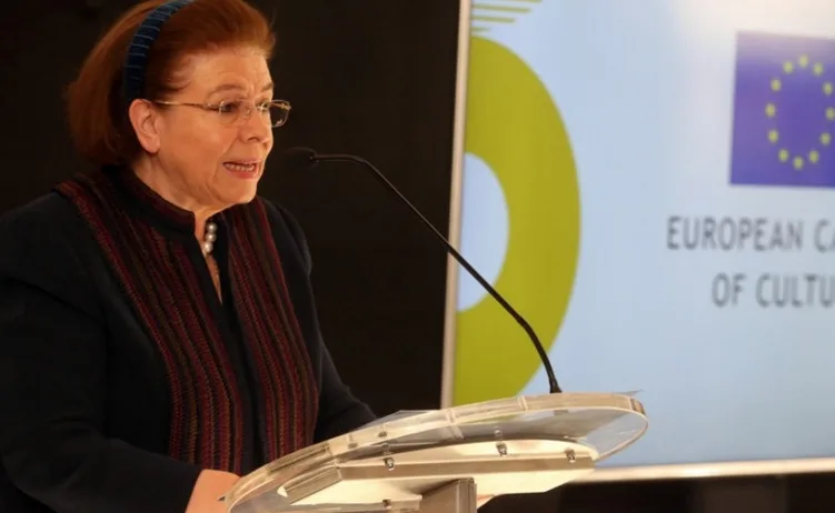 Žena u naočarima i sa maramom oko vrata drži govor ispred postolja sa mikrofonom, sa logom Evropske unije i natpisom "European Capital of Culture" u pozadini.