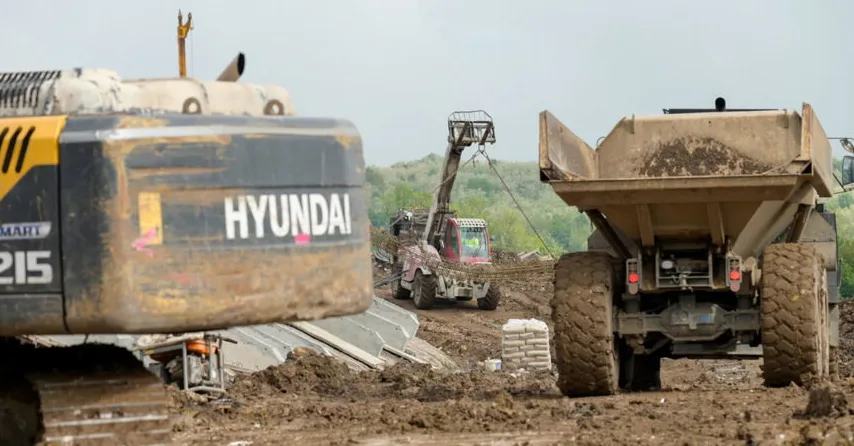Bager marke Hyundai sa brojem 215 u prvom planu, pored njega kamion kiper i u pozadini teleskopski manipulator koji prenosi armaturu.