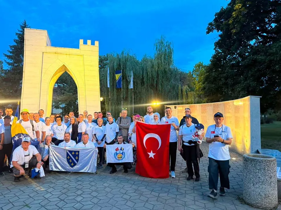 Grupa ljudi, odjevena u bijele majice, drži zastave Bosne i Hercegovine i Turske ispred Bijele tvrđave, spomenika u Potočarima.