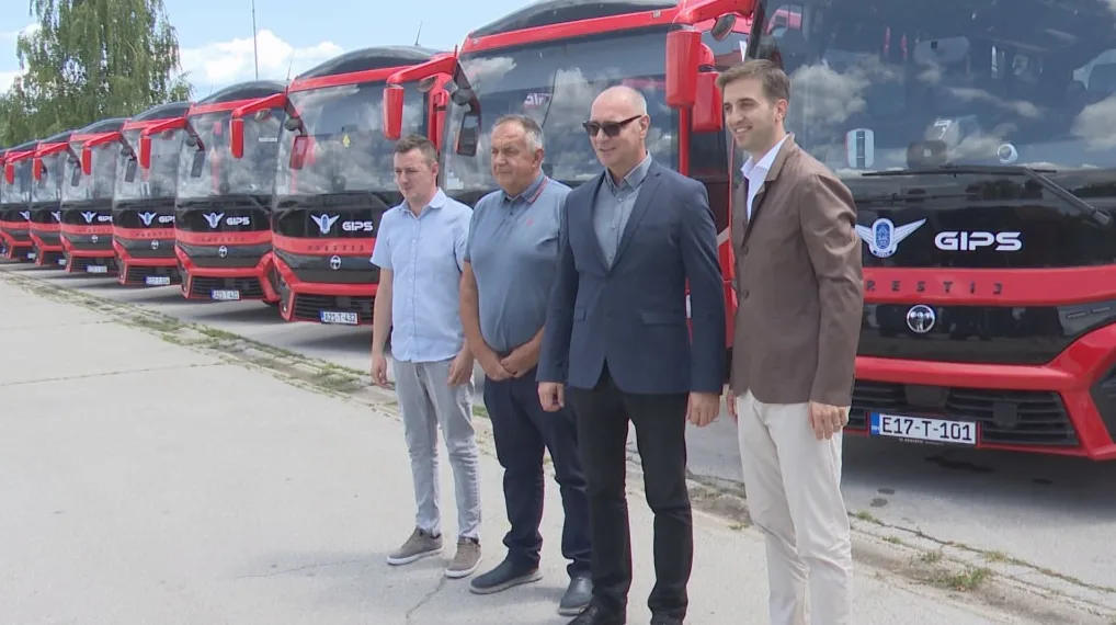 Grupa muškaraca u poslovnim odijelima stoji u redu ispred redova novih GIPS autobusa, parkiranih napolju.