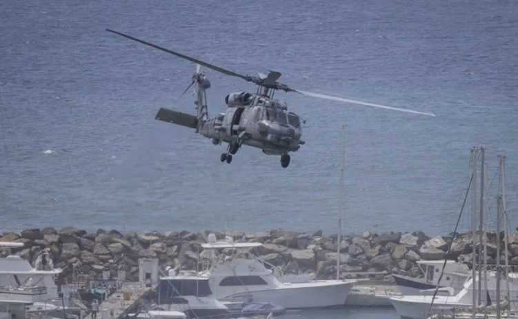 Vojni helikopter leti iznad mora, iznad marine s jahtama i brodicama.
