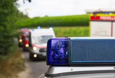 Plavo rotirajuće svjetlo na vozilu hitne pomoći u prvom planu, sa vatrogasnim vozilom i drugim vozilima hitne pomoći u pozadini na putu.