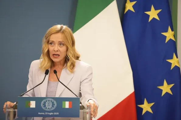 Žena u svijetlo-sivom sakou govori za govornicom, sa italijanskom i zastavom Evropske unije u pozadini.