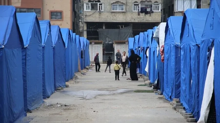 Ljudi prolaze kroz prolaz između redova plavih šatora u izbjegličkom kampu.