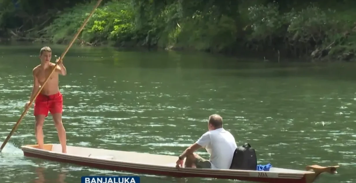 Mladić na kanuu vesla štapom na rijeci Vrbas, dok drugi čovjek sjedi u kanuu.