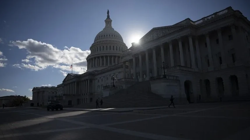 Ameriški Kapitol v Washingtonu DC, z vzhajajočim soncem, ki sije skozi kupolo, in zastavo ZDA na pol droga.