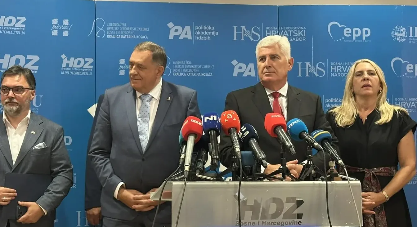 Četiri osobe stoje iza stalka s mikrofonima ispred plave pozadine s logotipima HDZ-a i drugih srodnih organizacija.