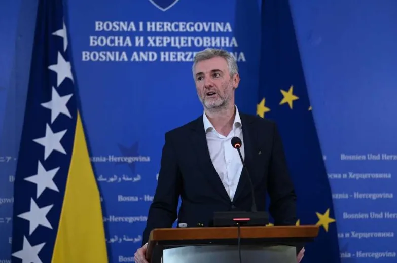 Političar sa sijedom kosom govori na konferenciji za medije, stojeći iza govornice ispred zastave Bosne i Hercegovine i Evropske unije.