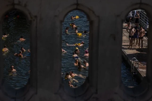 Grupa ljudi uživa u kupanju u rijeci tokom sunčanog dana, vidljivi kroz tri ukrasna otvora.