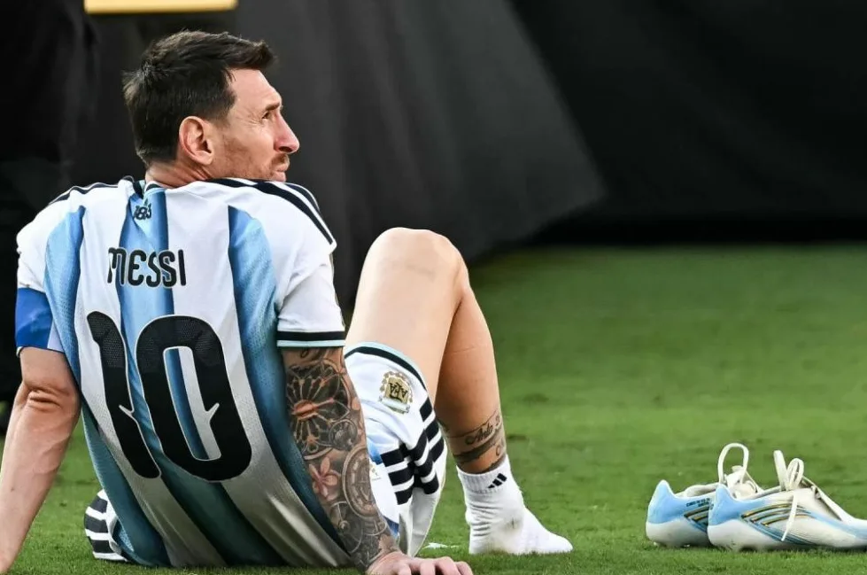 Lionel Messi sjedi na zelenom travnjaku, odjeven u dres argentinske nogometne reprezentacije s brojem 10 i imenom 'MESSI' ispisanim na leđima.