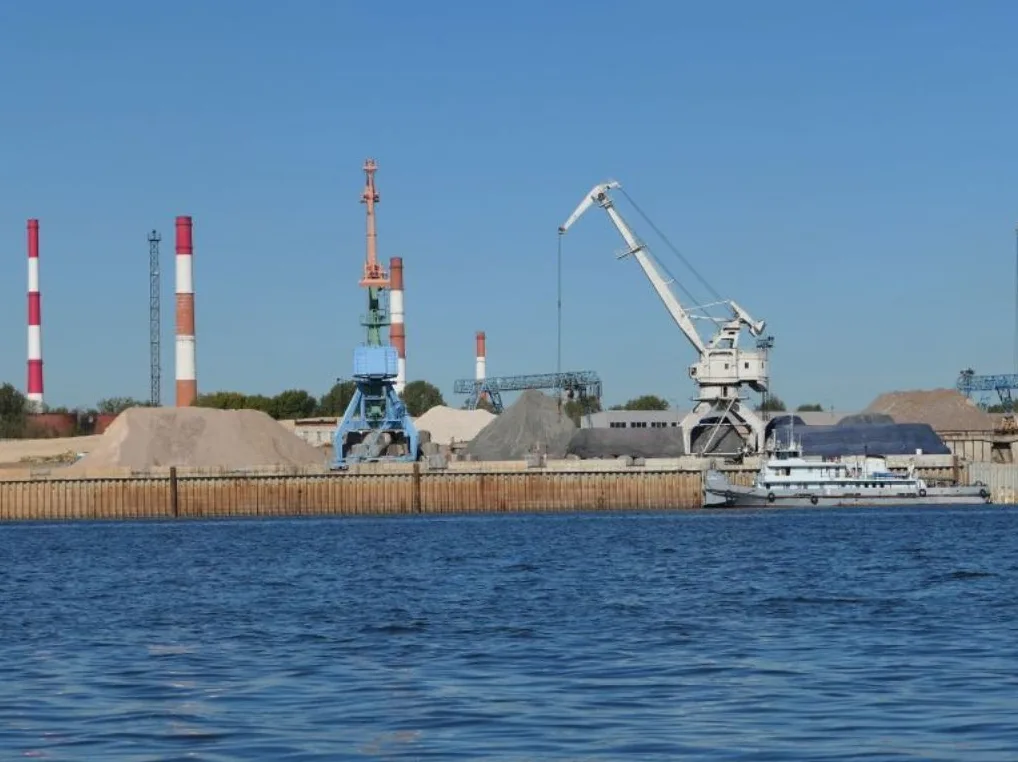 Industrijski pejzaž luke sa velikim dizalicama, dimnjacima i brodom na vodi.