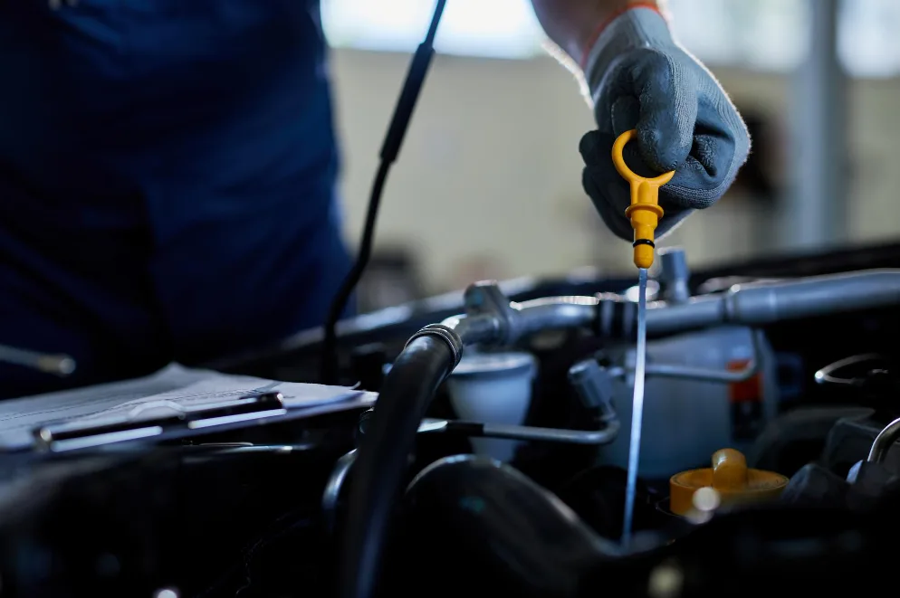 Mehanicar u radionici provjerava nivo ulja u automobilu pomocu mjernjacce.