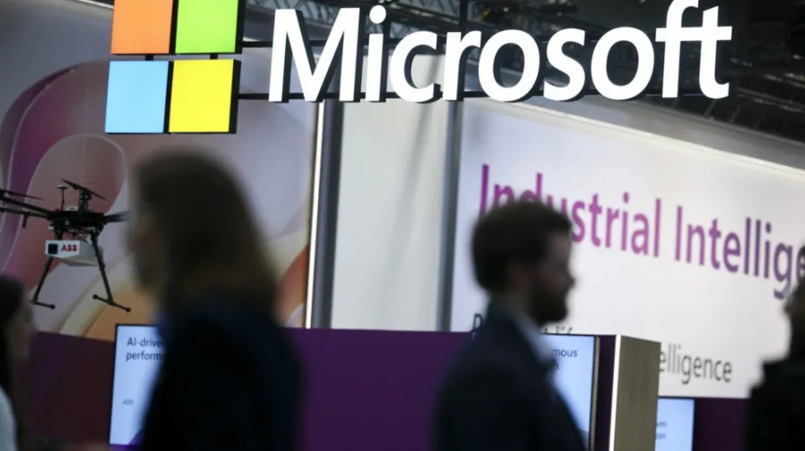 Logo Microsofta iznad natpisa "Industrial Intelligence" na izložbenom štandu, sa dronom i prikazom "AI-driven performance" u prvom planu.