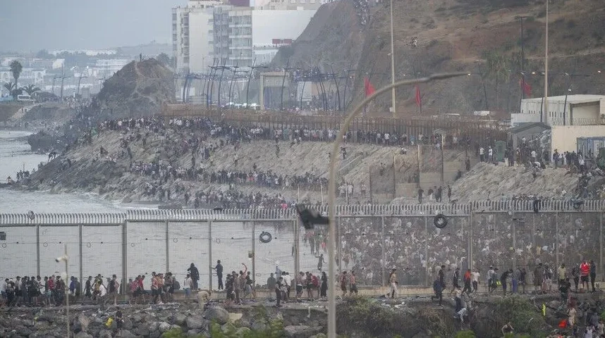 Veliki broj migranata pokušava preći visoku ogradu na granici, neki su se popeli na stijene pored ograde.