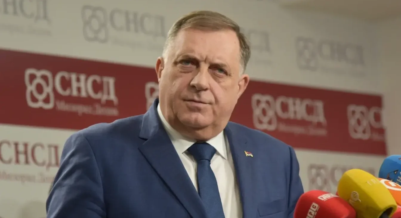 Političar Milorad Dodik nosi plavo odijelo i plavu kravatu, a iza njega se vidi logotip SNSD-a.