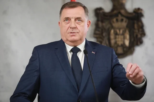 Milorad Dodik u tamnom odijelu i tamnoj kravati govori za govornicom, s grbom iznad glave.