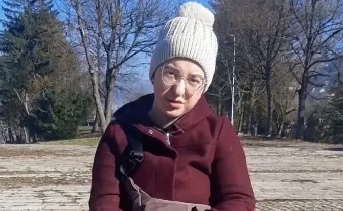 Mlada djevojka u zimskoj jakni i kapi odaje izgled sa osmijehom dok stoji na otvorenom.