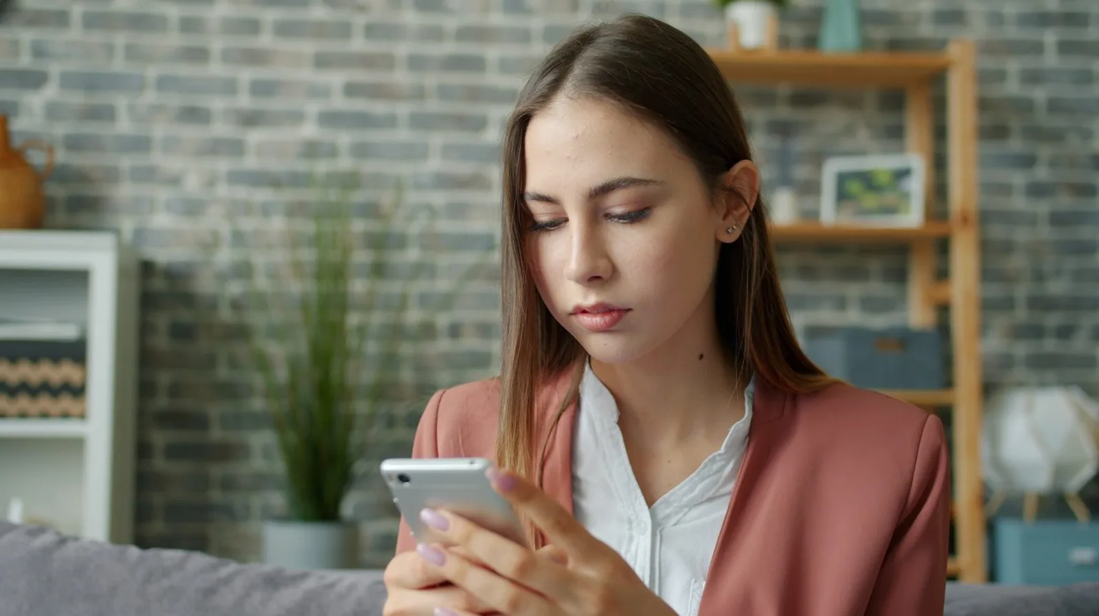 Mlada žena u roze sakou gleda u svoj pametni telefon dok sjedi na kauču.