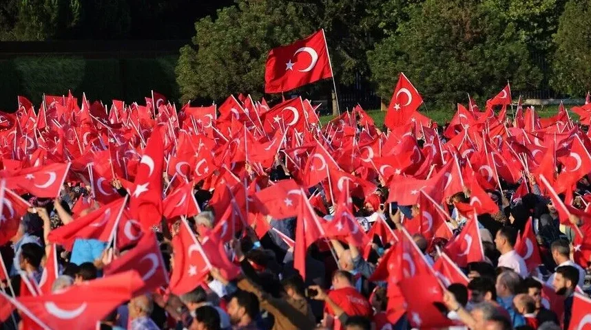 Veliko mnoštvo ljudi drži turske zastave u vazduhu, simbolizujući nacionalno okupljanje i patriotizam.