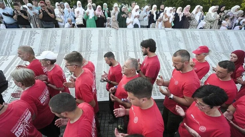 Ljudi u crvenim majicama i žene u hidžabima mole se ispred spomen-ploče sa imenima žrtava