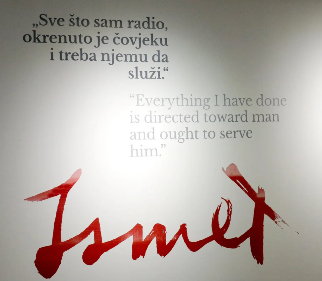 Citati na bosanskom i engleskom jeziku iznad stiliziranog, crvenog, rukom pisanog potpisa "Ismet".