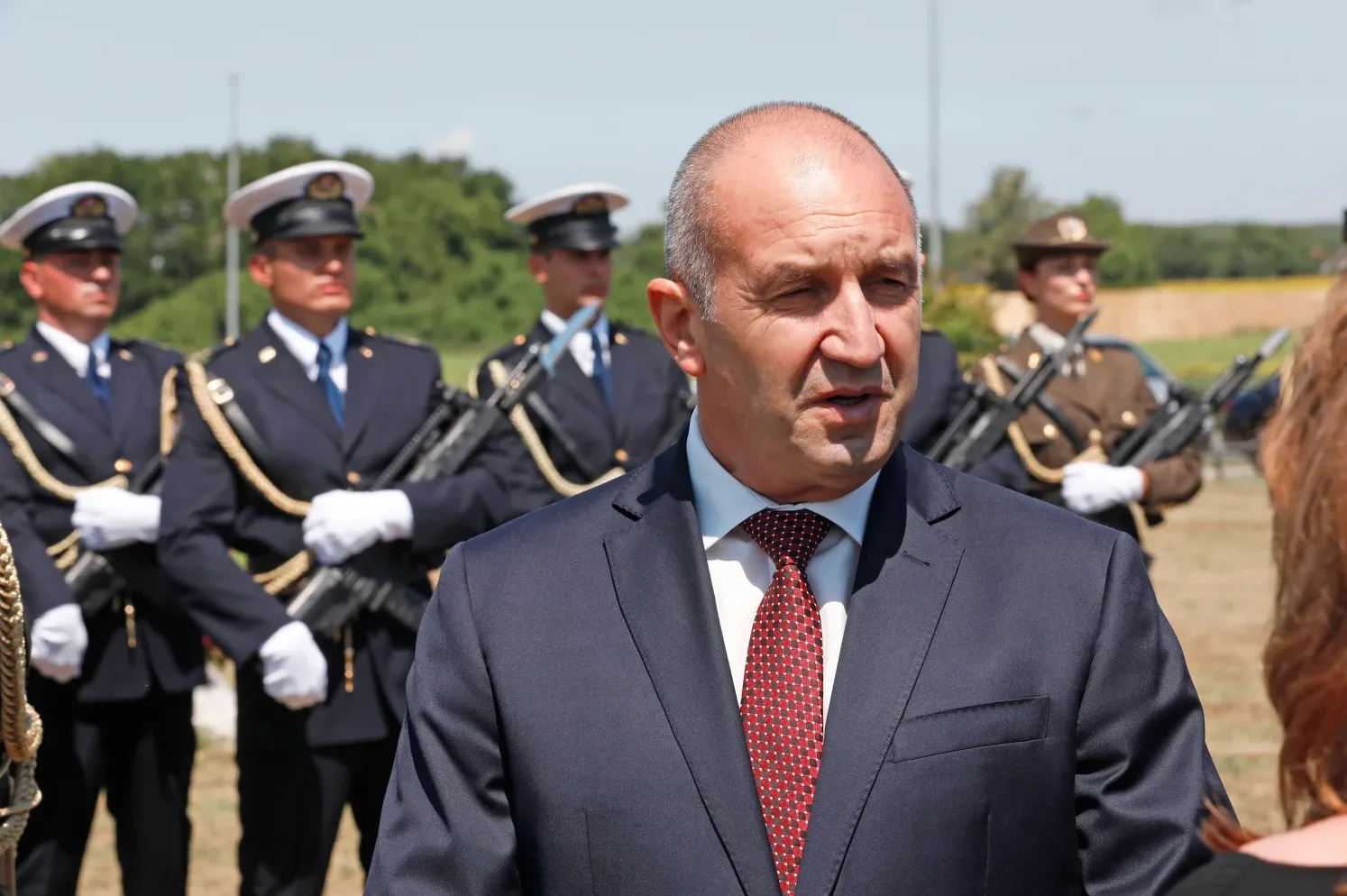 Predsjednik Rumen Radev u tamnom odijelu i crvenoj kravati, ispred reda vojnika u tamnoplavim uniformama i vojnikinje u smeđoj uniformi.