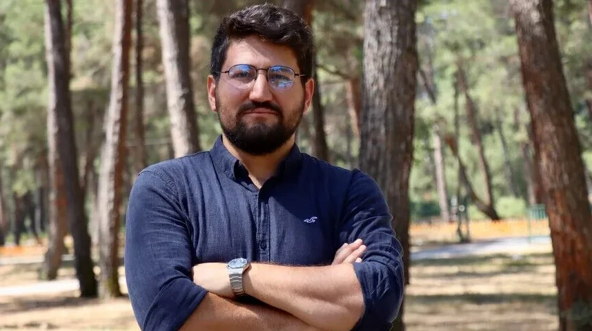 Muškarac s naočalama i bradom gleda u kameru, ruku sklopljenih, u parku