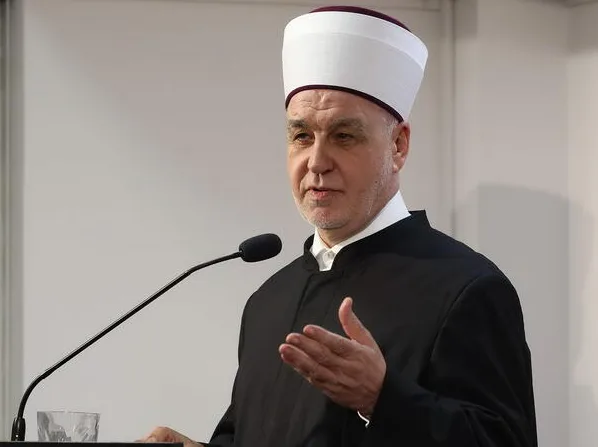 Muslimanski dužnosnik u bijeloj kapi i crnom odijelu govori iza mikrofona.