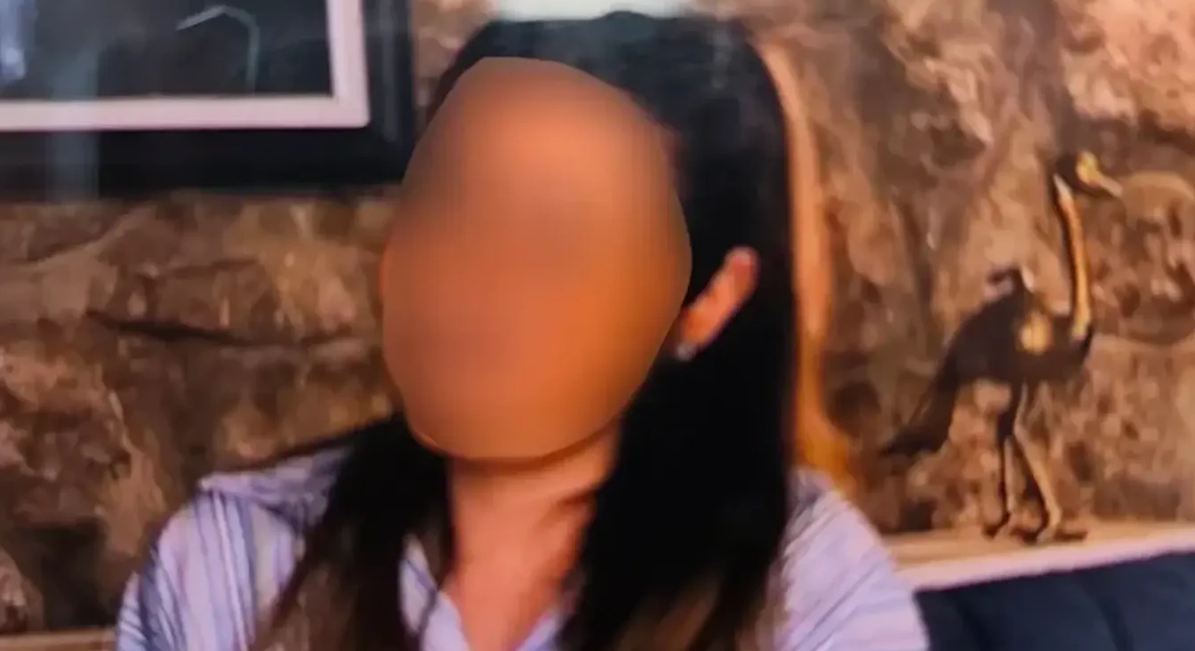 Fotografija prikazuje neizvjesnu osobu sa zamućenim licem, odjevenu u prugastu košulju. U pozadini se vidi dekorativna figura ptice nalik noju, postavljena ispred zida imitacije kamena.