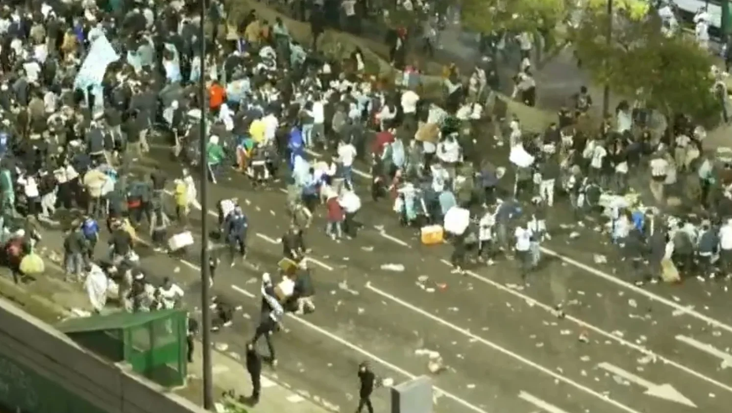 Velika grupa ljudi na ulici, neki nose zastave, drugi nose predmete, a na ulici ima dosta smeća.