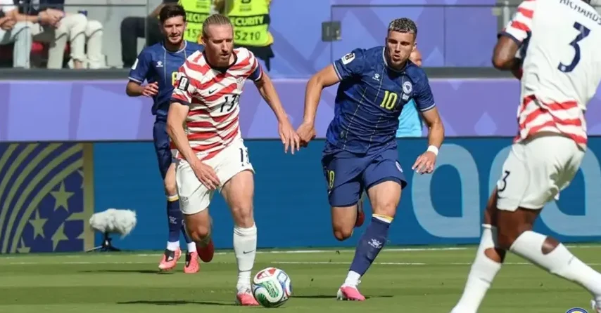 Fudbalski savez SAD-a (USSF) branič s brojem 17 drži za ruku igrača sa brojem 10, koji nosi tamnoplavi dres.